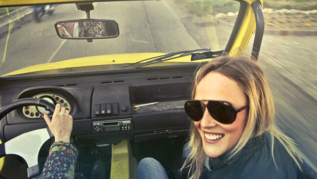 A woman, who happens to be a driver, is driving a yellow car.