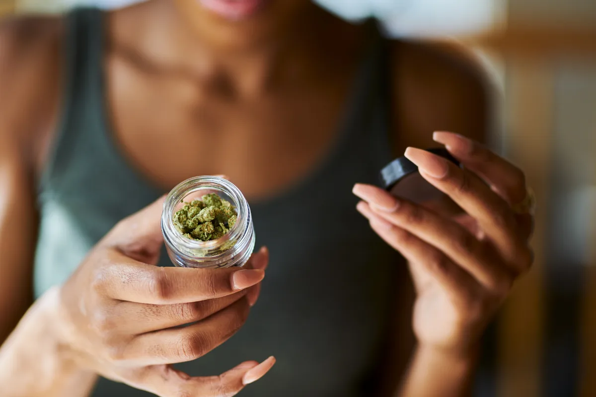 A person holding an open jar of cannabis buds.