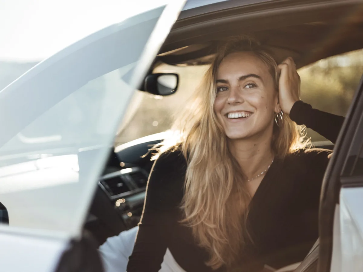 Woman smiling and adjusting her hair while sitting in a car.