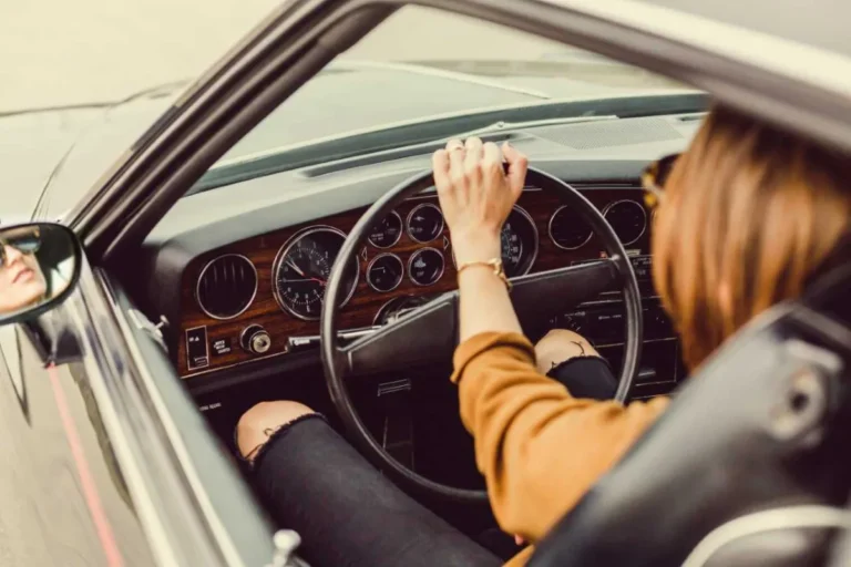 A person driving a vintage car with hands on the steering wheel and a view of the dashboard.