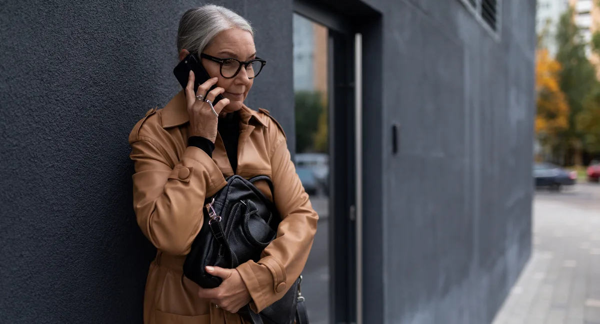 Elderly woman in glasses using a smartphone on a city street.