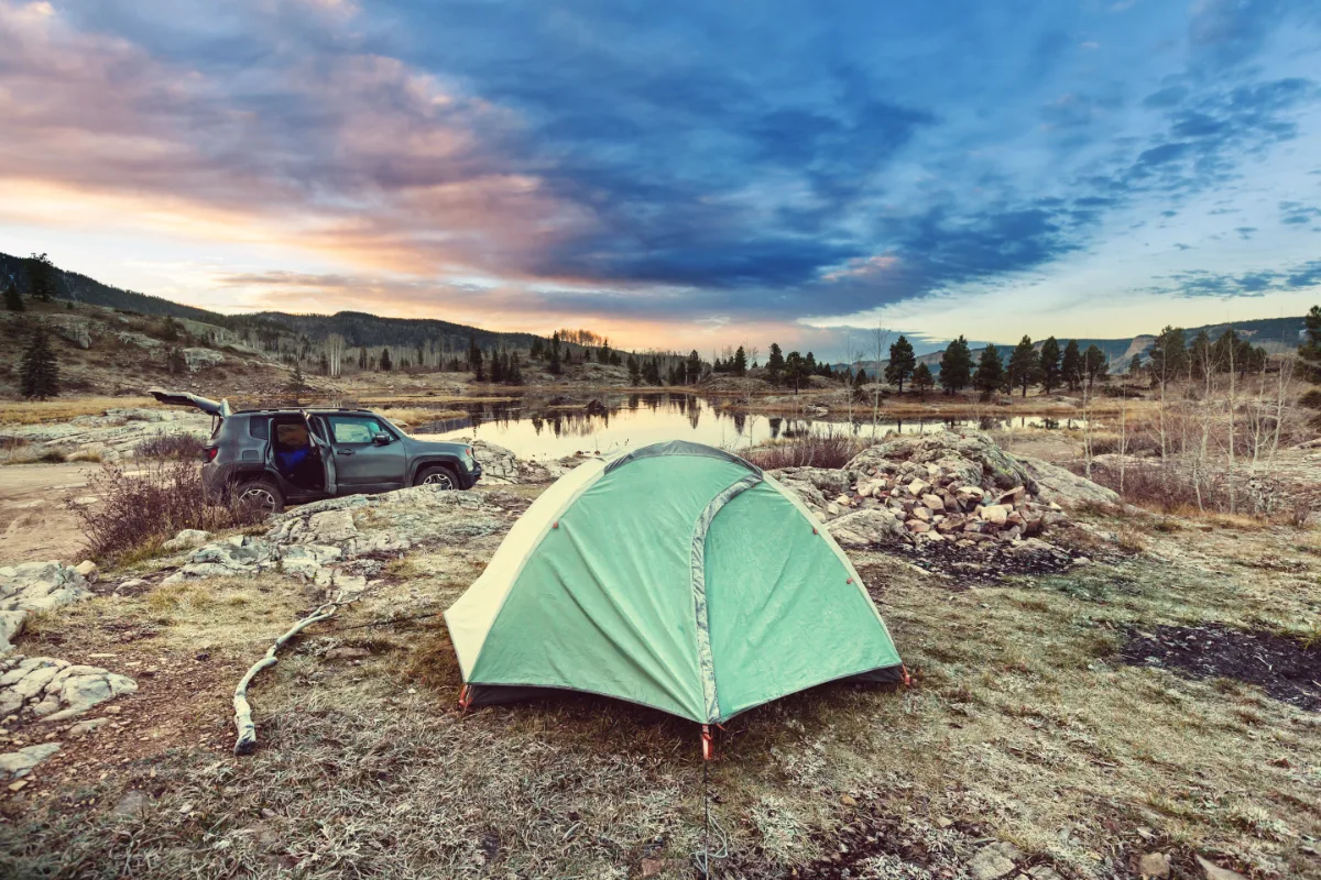 A tent is set up near a lake at sunset, providing the perfect backdrop for a tranquil evening.