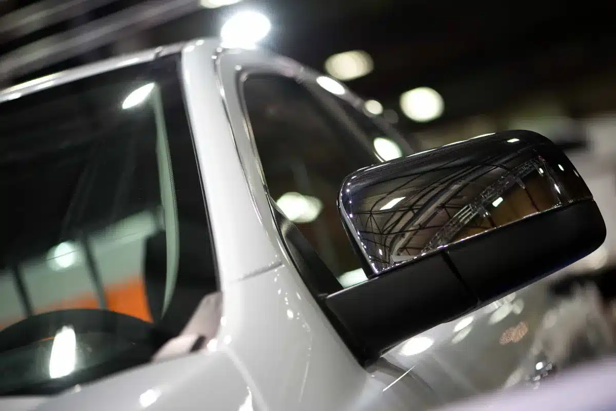 A side view mirror of a white car at an auto show.