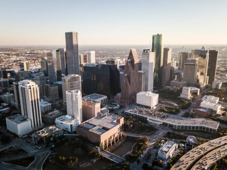 Aerial view of a modern downtown skyline in Texas bathed in warm sunlight with shadows stretching over the urban landscape.