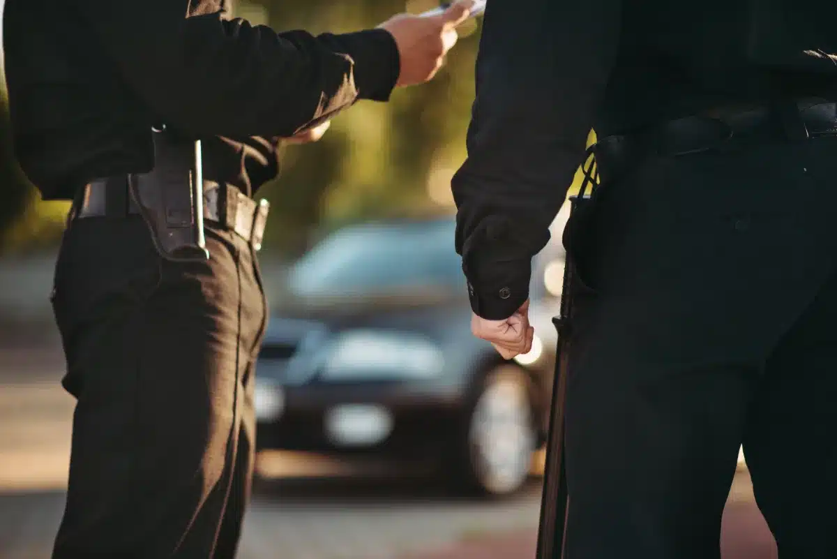 Two police officers standing next to a car conduct investigations related to a misdemeanor offense, ensuring the constitutional rights of the individuals involved.