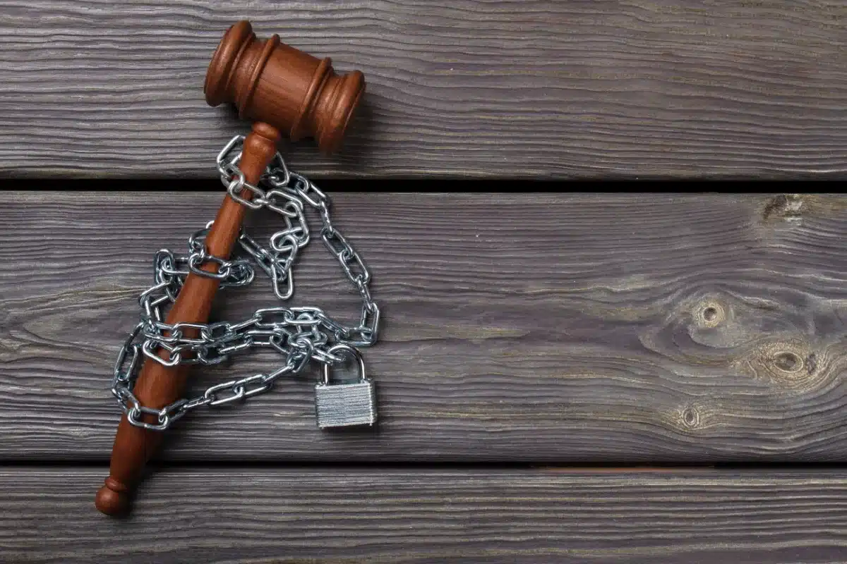 A wooden gavel with chains and a padlock on a wooden background, symbolizing charges and probation.