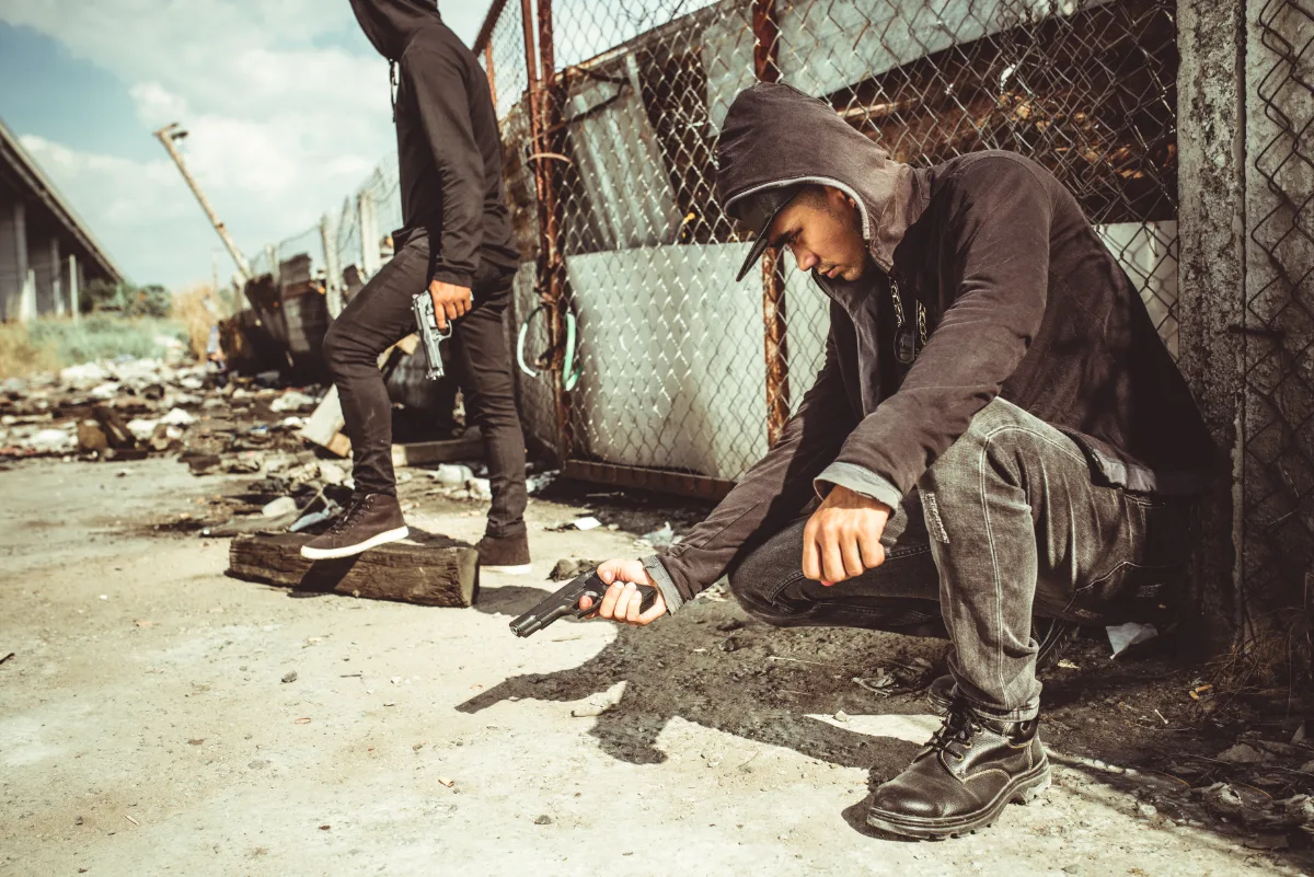Two people in hoodies in an urban environment with one crouching and reaching toward the ground.