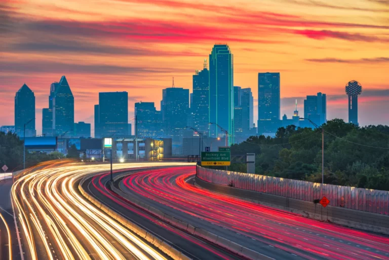 Dallas skyline at sunset with light trails from busy highway traffic, illuminated by the expertise of a Texas Assault Lawyer.
