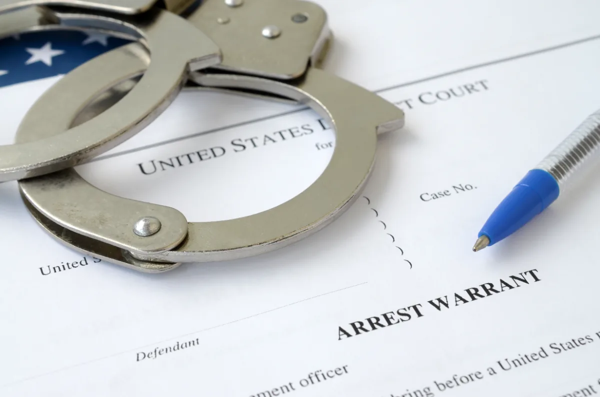 A pair of handcuffs and a pen on top of an arrest warrant for a misdemeanor offense.