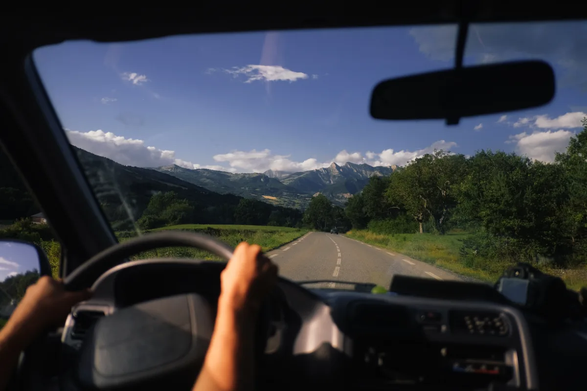 A driver navigating a car on a road with breathtaking mountains in the background.