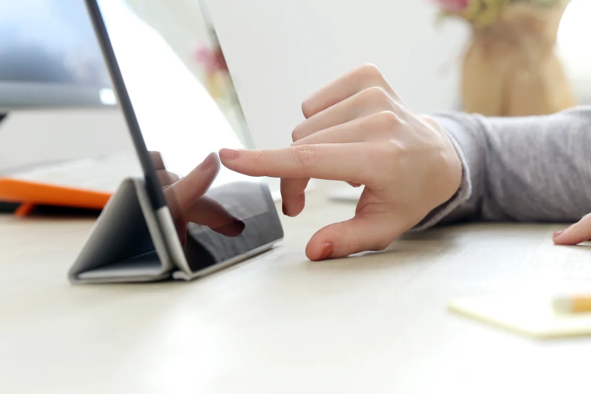 A woman's hand is pointing at a tablet computer.