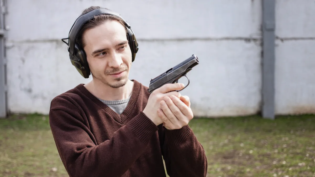 Man with hearing protection handling a handgun at an outdoor shooting range.