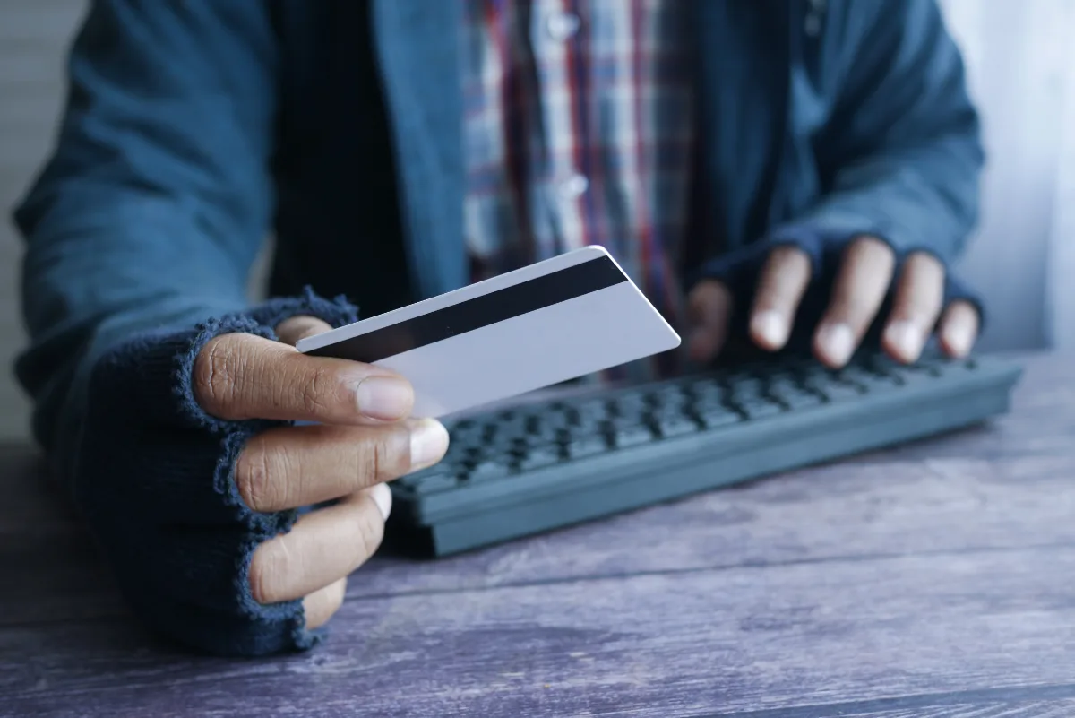A man is holding a credit card and typing on a keyboard to complete a transaction.