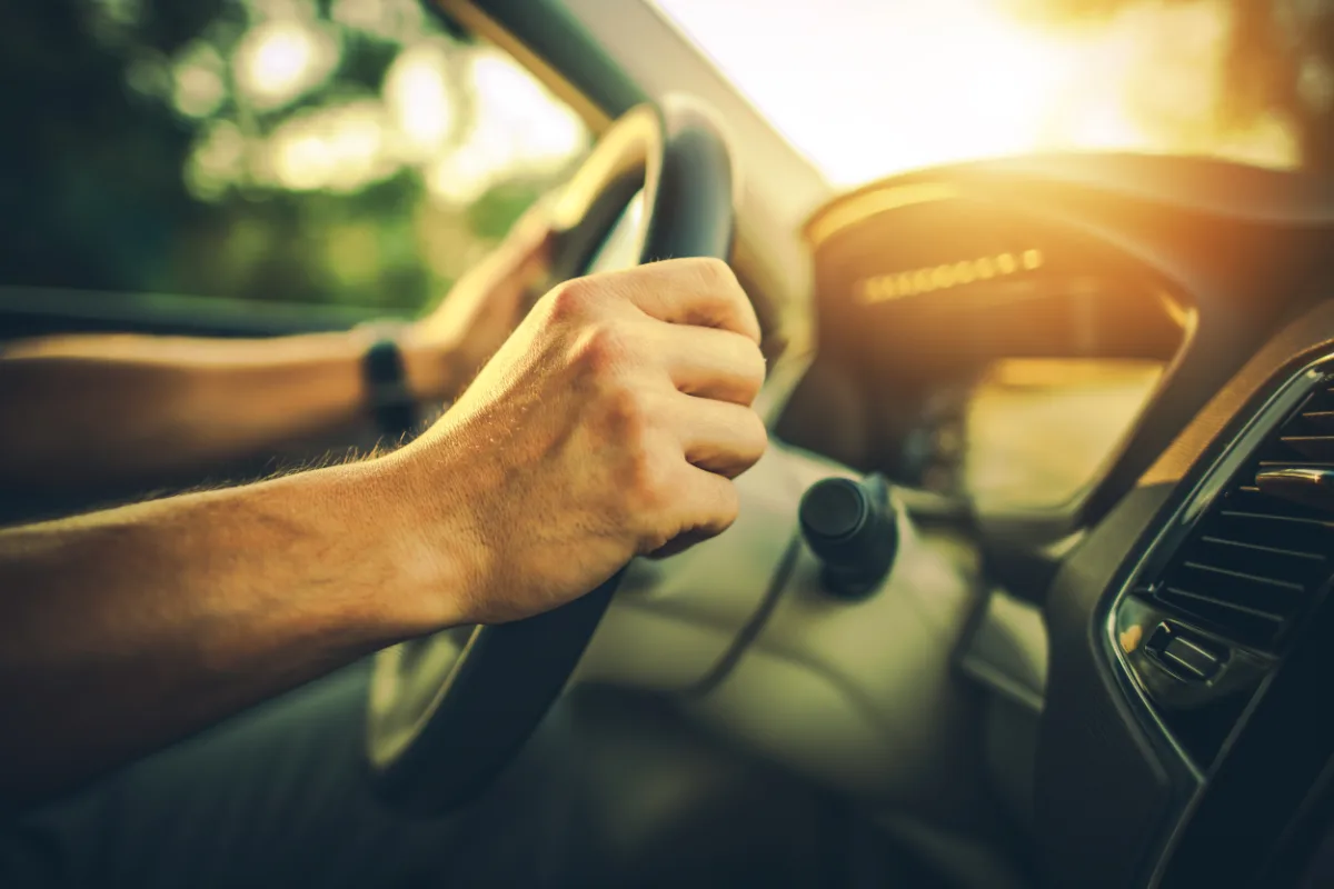 Close-up of a person's hands gripping a steering wheel, with sunlight streaming through the car window, reminiscent of a scene in Texas.