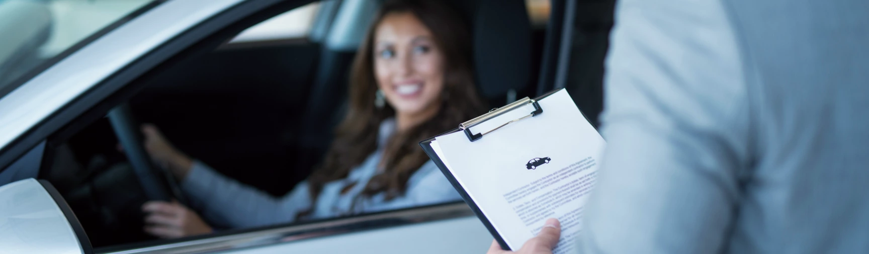 Woman in car interacting with person holding clipboard with vehicle document.