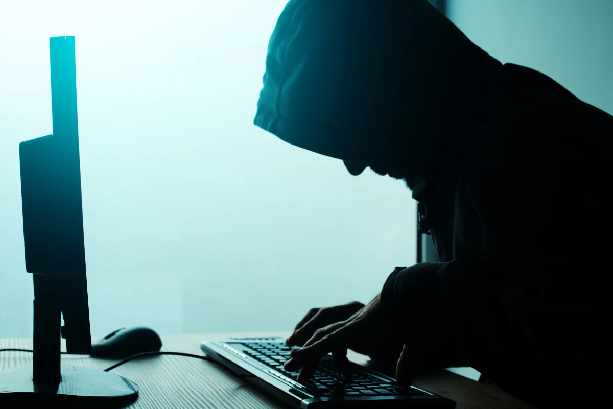 A person in a hoodie typing on a computer while facing probation charges.
