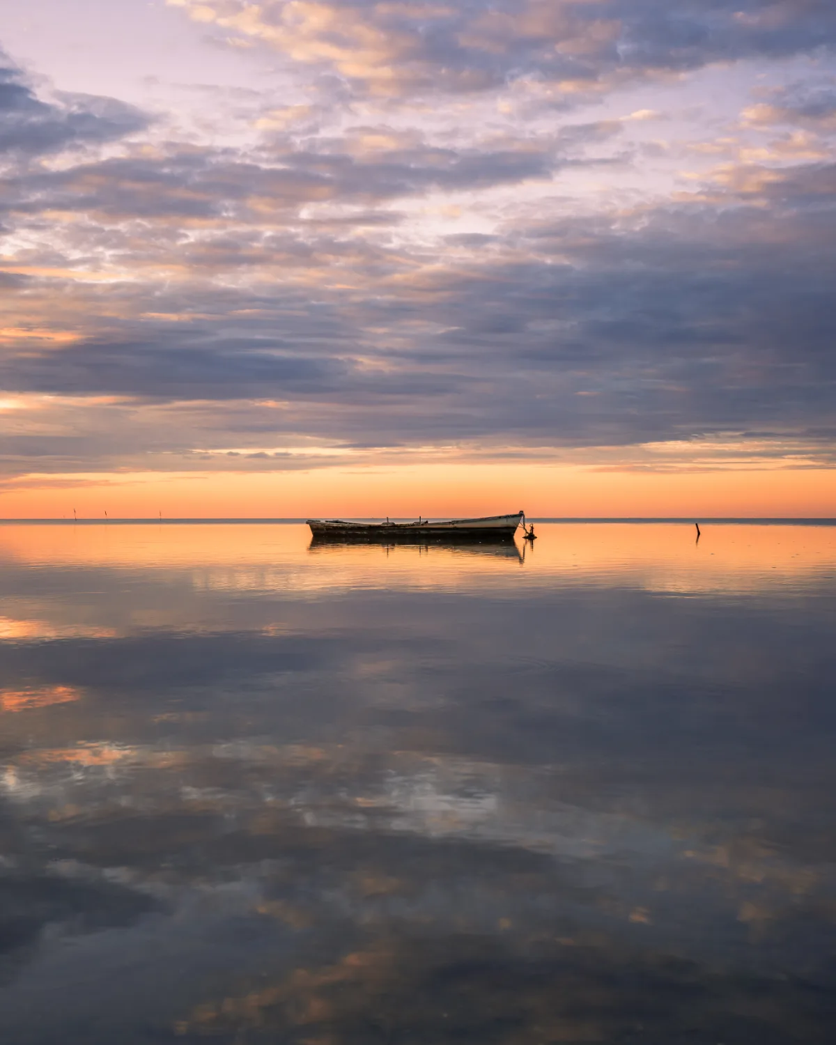 A canoe peacefully drifts in calm water at sunset.