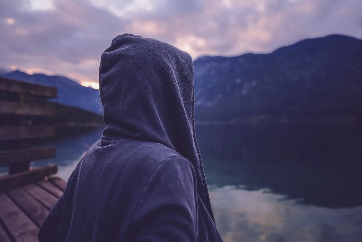 A person in a hoodie overlooking a serene lake, pondering the potential consequences of their misdemeanor charge and contemplating whether they need legal representation from a skilled lawyer.
