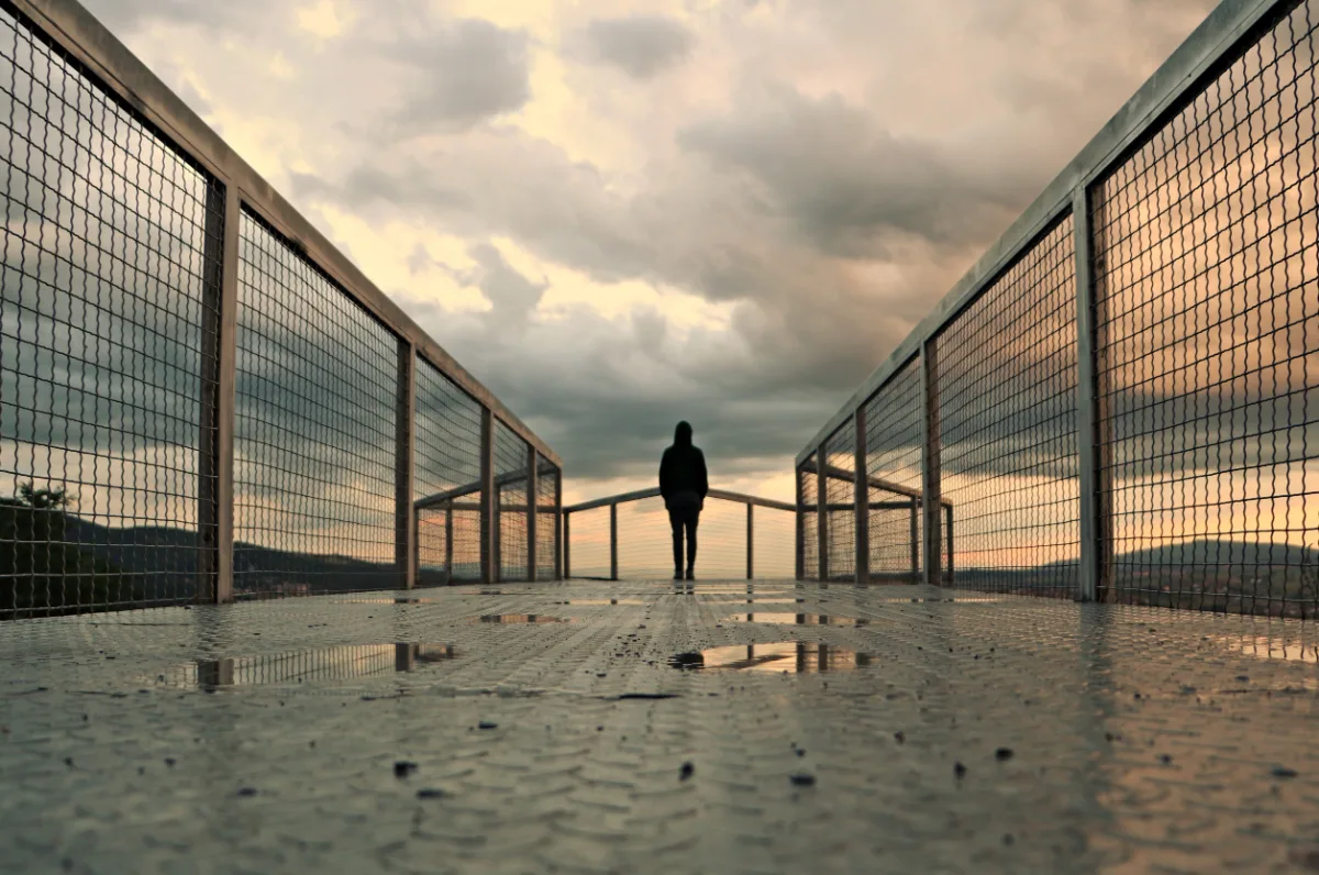 A person is standing on a bridge with a cloudy sky, contemplating a misdemeanor.