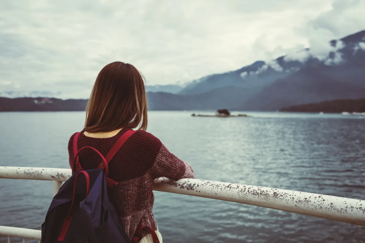 A woman with a backpack enjoying the serene view of a lake.