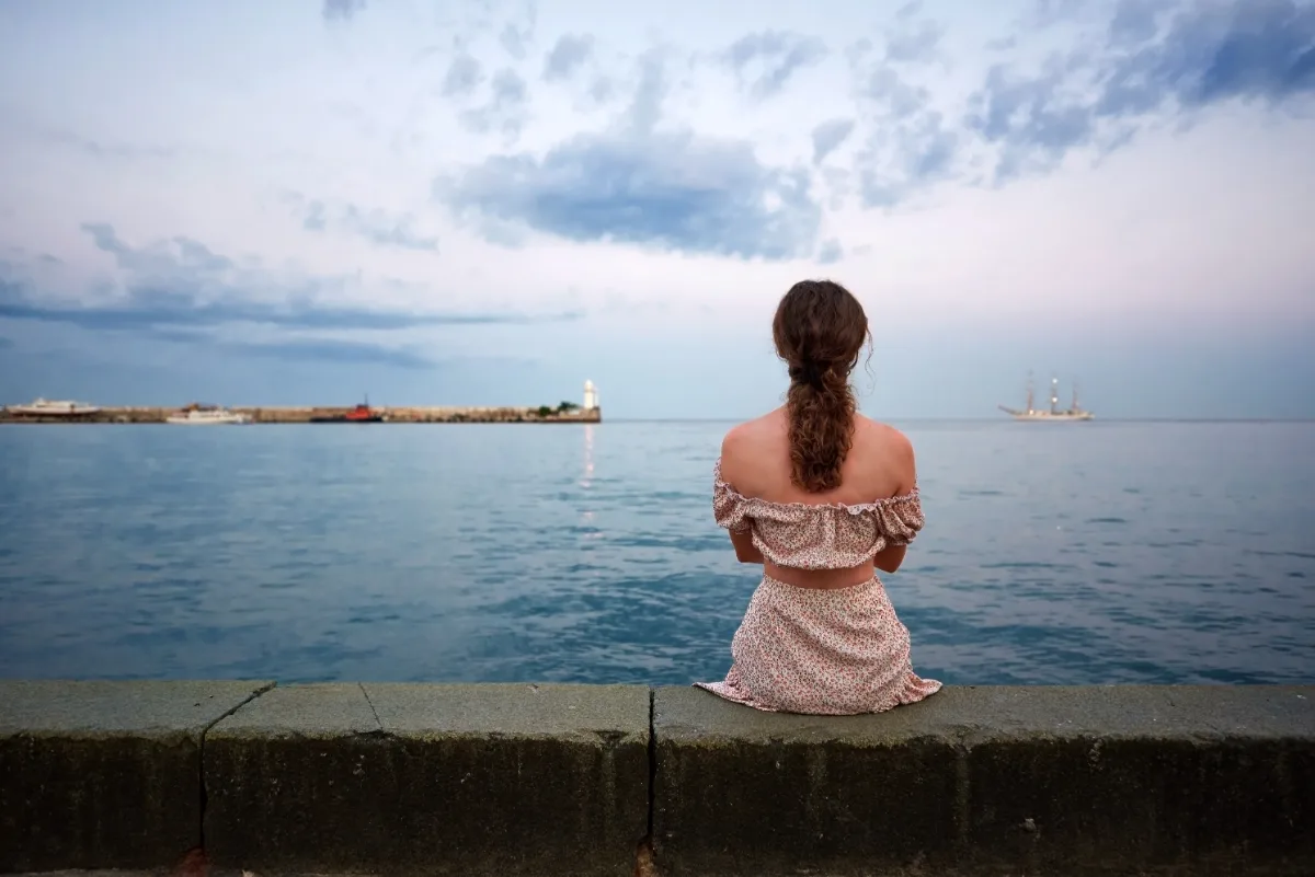 A woman sitting on a wall by the ocean, deep in thought about potential constitutional charges, while consulting with her lawyer.