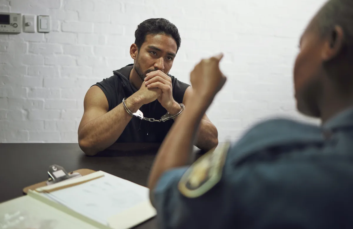A man in handcuffs being interrogated by a police officer at a table.