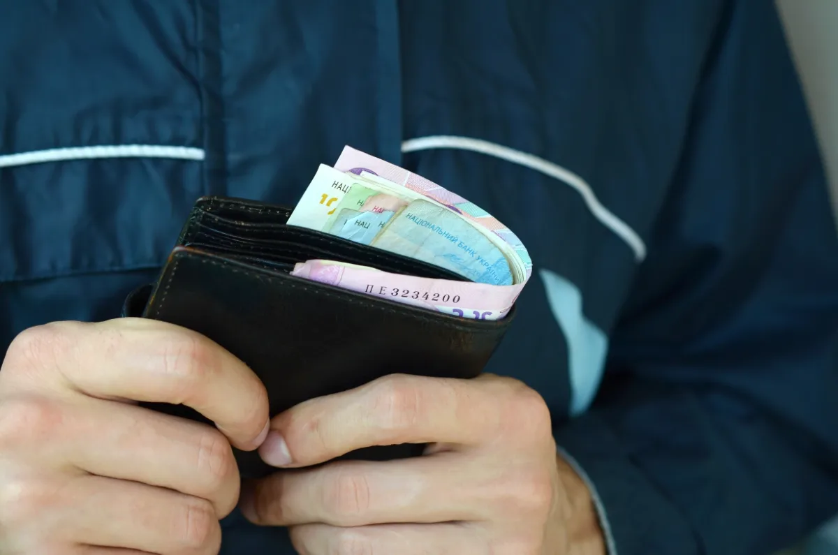 A man is holding a wallet full of money as he navigates charges involving financial transactions.