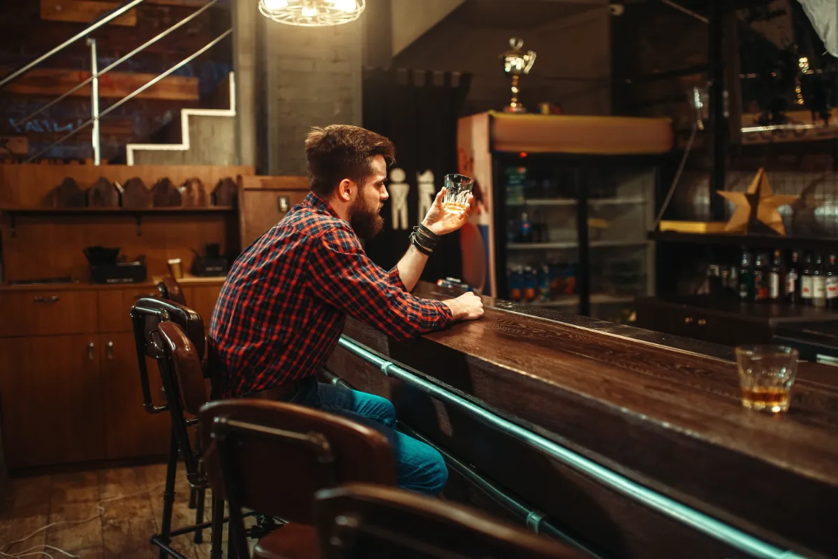 Man sitting at a bar counter holding a glass of whiskey.