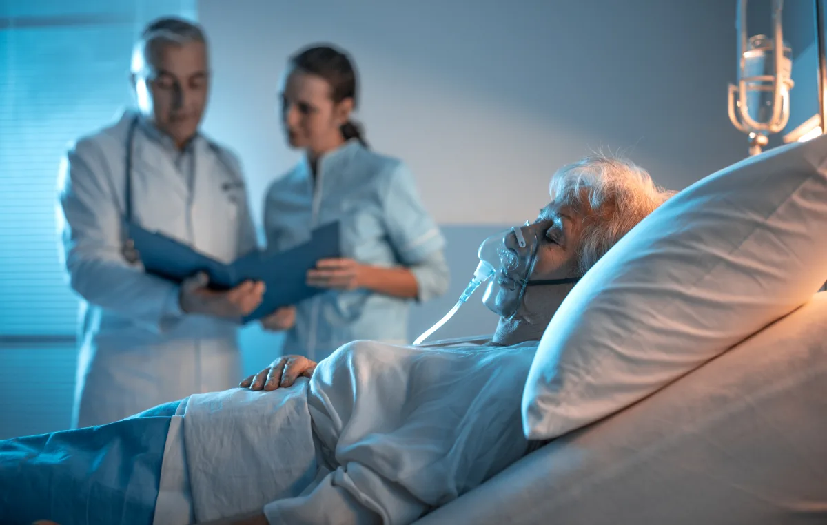 A woman is lying in a hospital bed with a doctor looking at her, possibly addressing her medical condition.