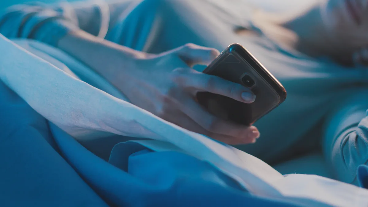 A woman laying in bed while browsing her cell phone.
