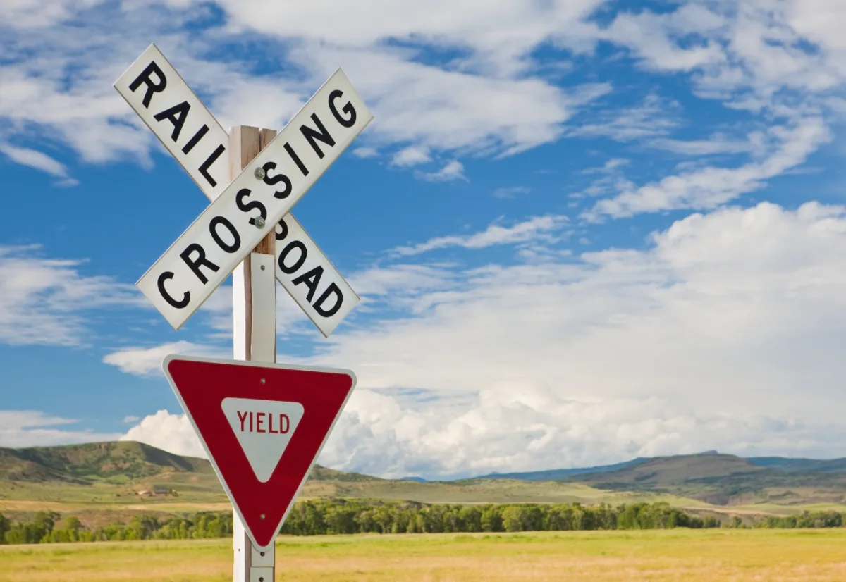 A railroad crossing sign in the middle of a field, alerting drivers to be cautious.