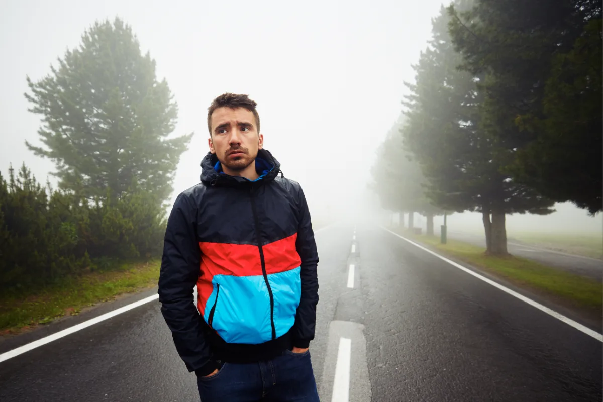 Man standing on a foggy road with hands in pockets.