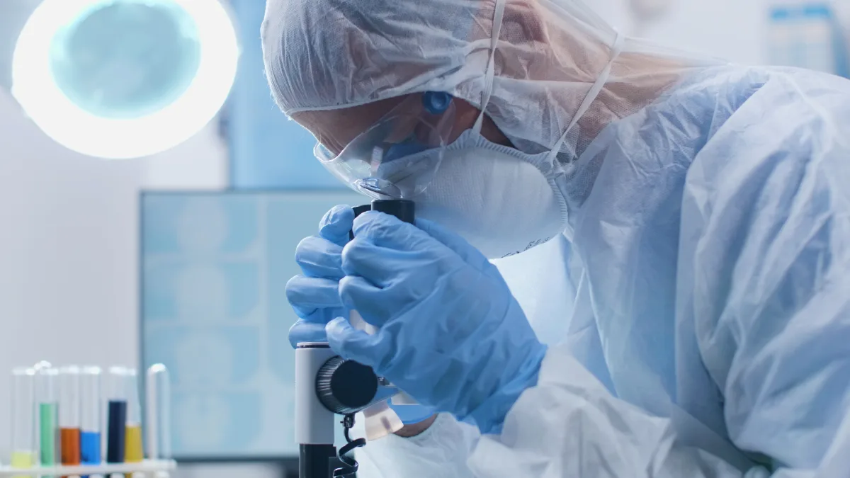 A man in a lab coat, possibly a scientist or researcher, is focusing intently on examining something under a microscope.