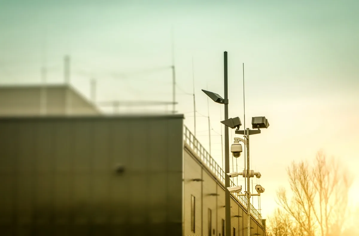 A group of surveillance cameras on a building at sunset, capturing potential evidence for a legal case involving a misdemeanor offense with constitutional implications that may require the expertise of a lawyer.
