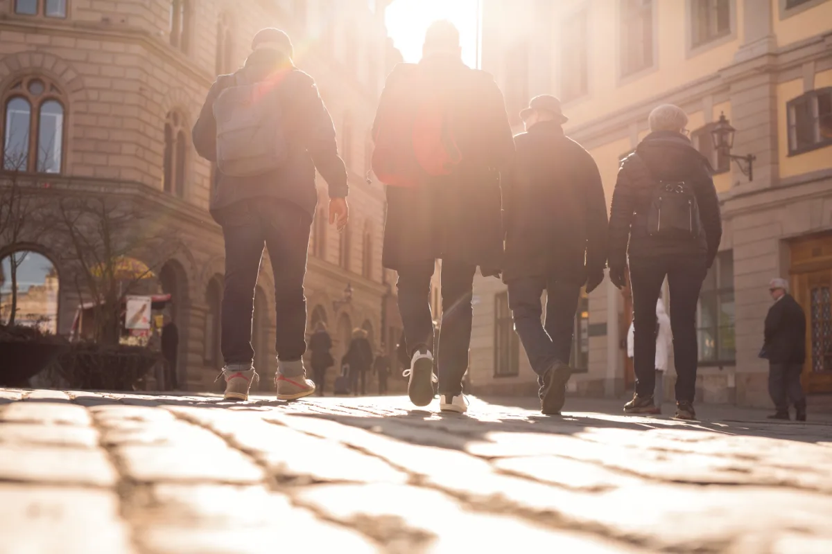 Four people walking on a cobblestone street, backlit by the sun.