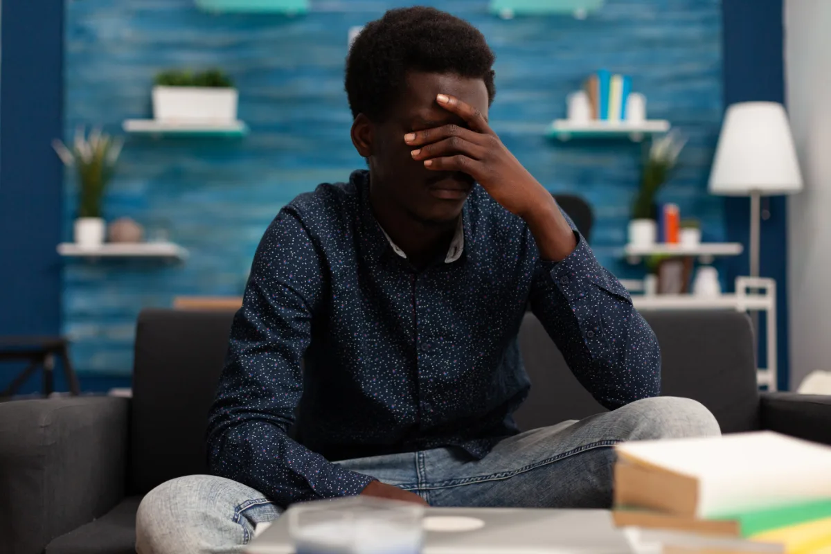 A black man sitting on a couch with his hand covering his face, potentially reflecting the emotional toll of a misdemeanor or probation.