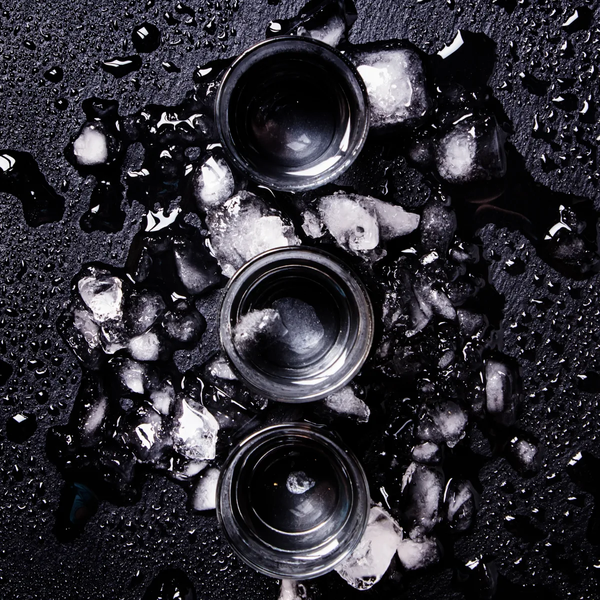 Three glasses of ice on a black surface.