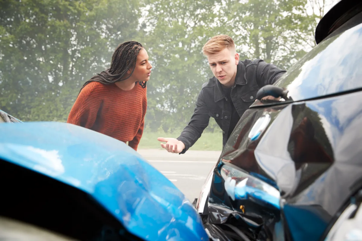 Two individuals engaging in a discussion beside damaged cars after a traffic accident.