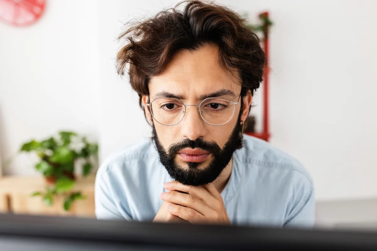 A focused man with glasses and a beard working at a computer.