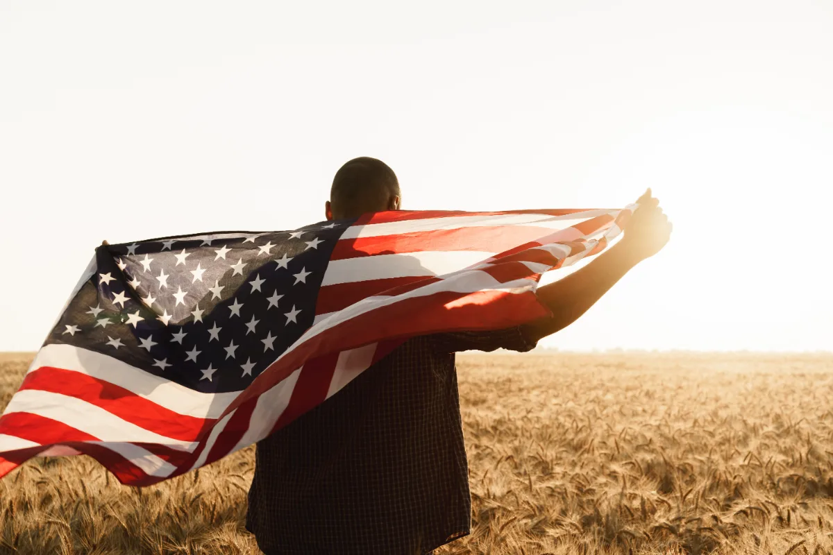 A man holding an American flag in a wheat field, displaying his patriotism.