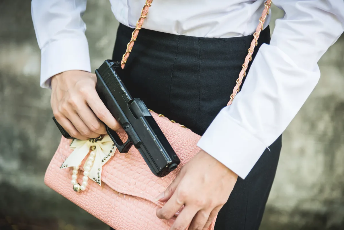 A person in a white shirt and black pants carrying a pink purse and a handgun.