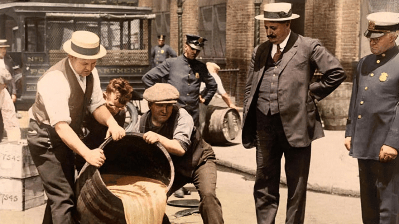 Men dumping out barrels under the supervision of police officers, likely during the prohibition era following the Eighteenth Amendment to the United States Constitution.